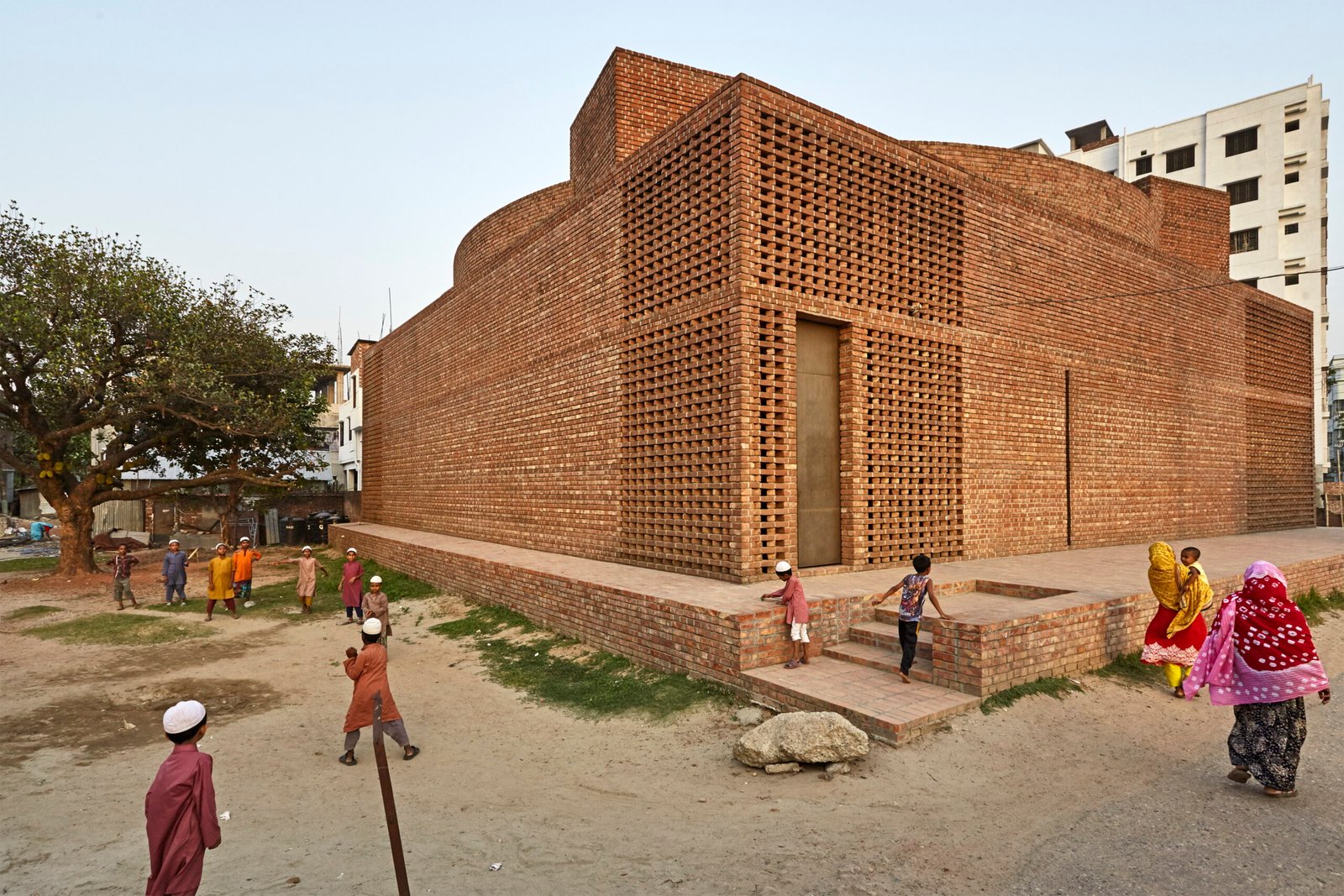 Exterior view of the Bait Ur Rouf Mosque showing the raised plinth, perforated brick walls, and neighborhood children