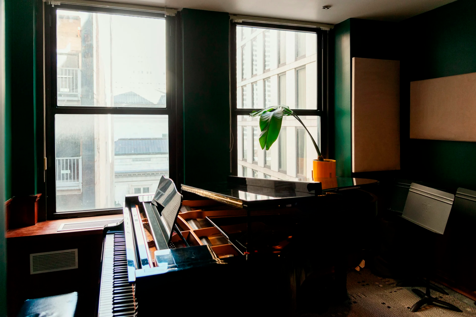 Grand piano with open score in a dark-walled room, natural light through urban windows