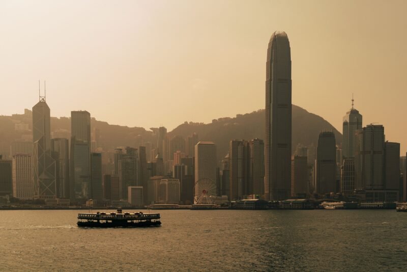 Hong Kong Island seen across Victoria Harbour in a warm haze, a ferry crossing in the foreground.